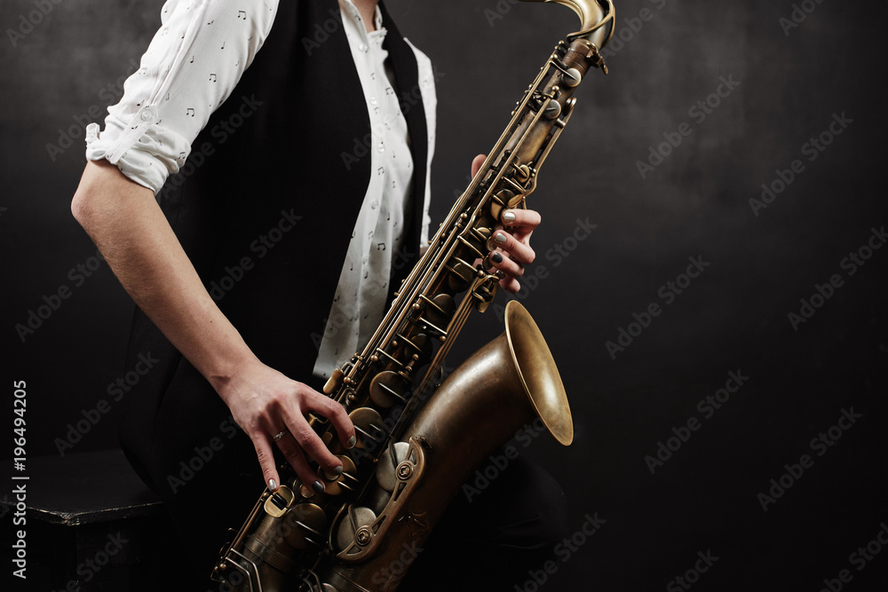 Obraz premium Young woman with saxophone on black background