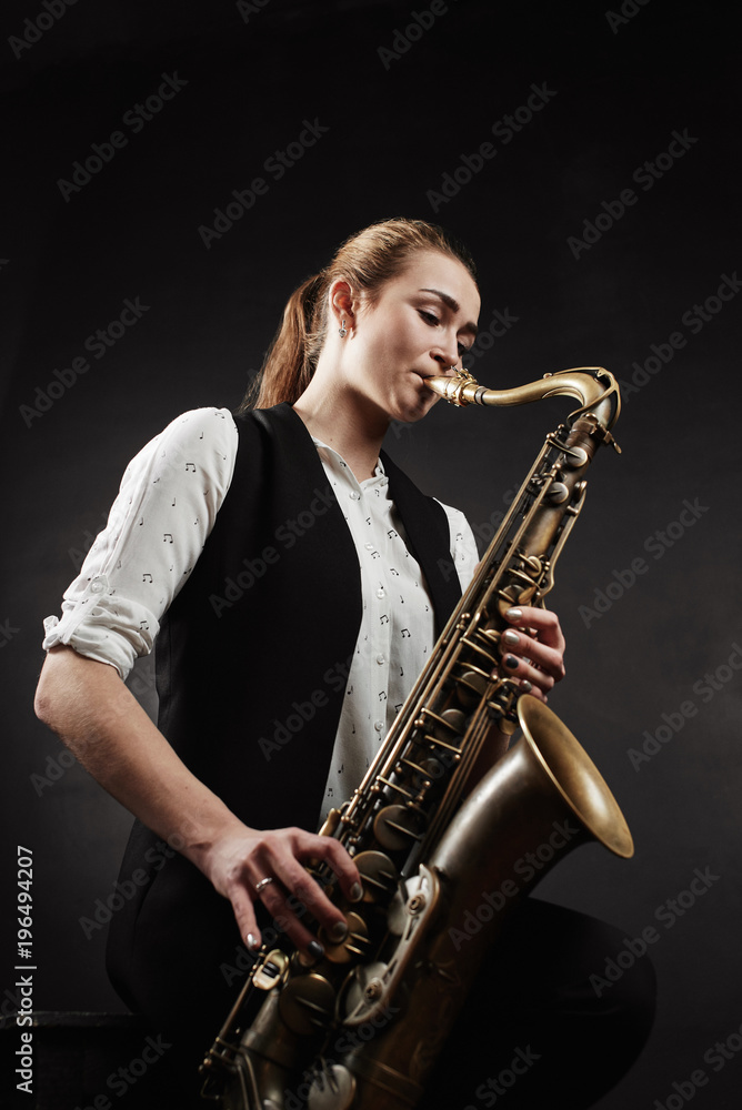 Obraz premium Young woman with saxophone on black background
