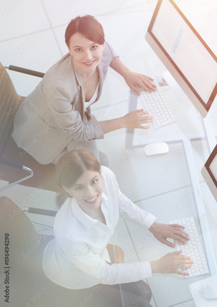 two business women sitting at Desk and looking at camera. - obrazy, fototapety, plakaty 