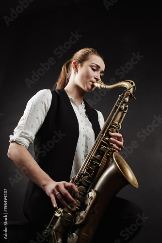 Young woman with saxophone on black background