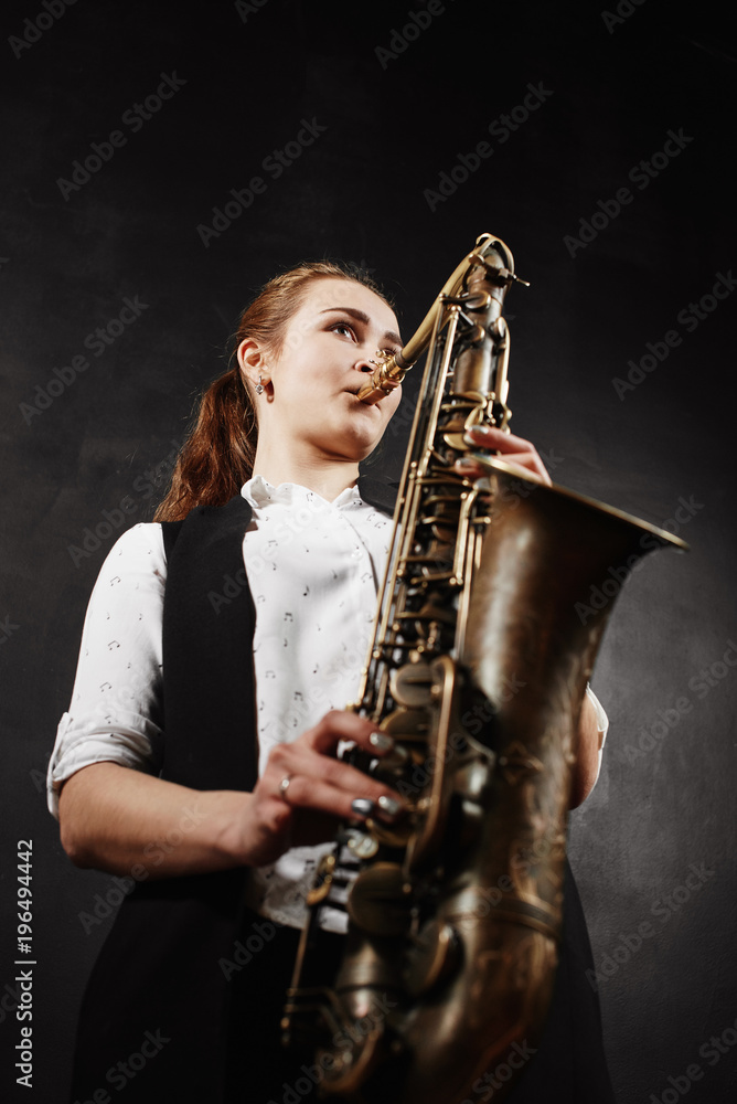 Fototapeta premium Young woman with saxophone on black background