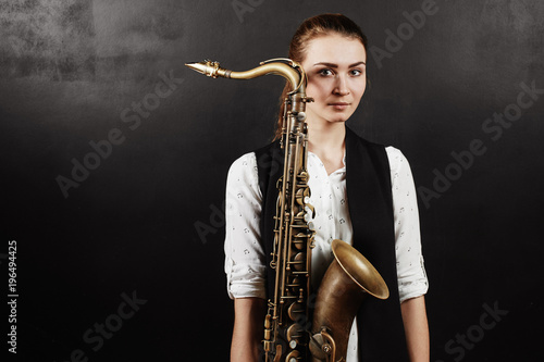 Young woman with saxophone on black background