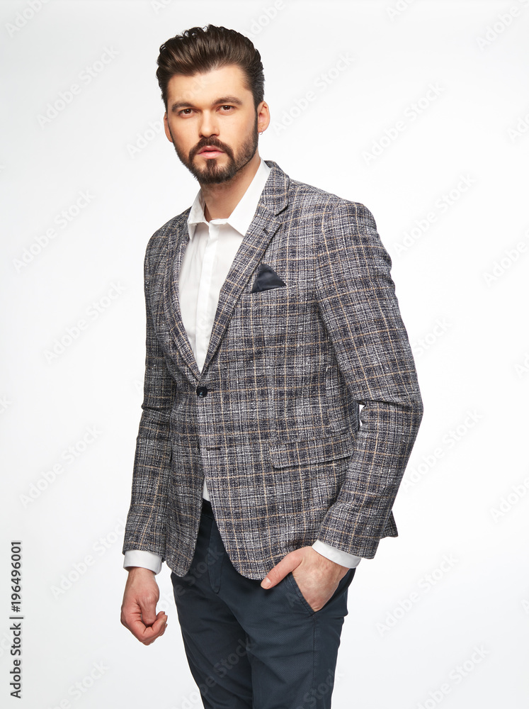 Fashion portrait of handsome male model with dark hair, beard and eyes, wearing white shirt, plaid grey jacket and dark pants, posing on white background Fashion portrait of handsome male model with dark hair, beard and eyes, wearing white shirt, plaid grey jacket and dark pants, posing on white background