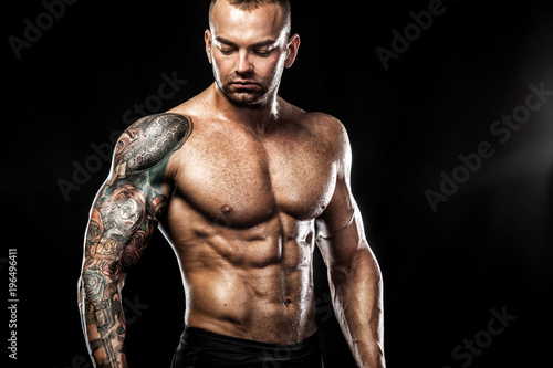 Handsome fit man posing wearing in jeans with tattoo. Sport and fashion concept isolated on black background.