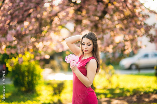 Beautiful girl posing to the photographer against the background of blooming pink trees. Spring. Sakura