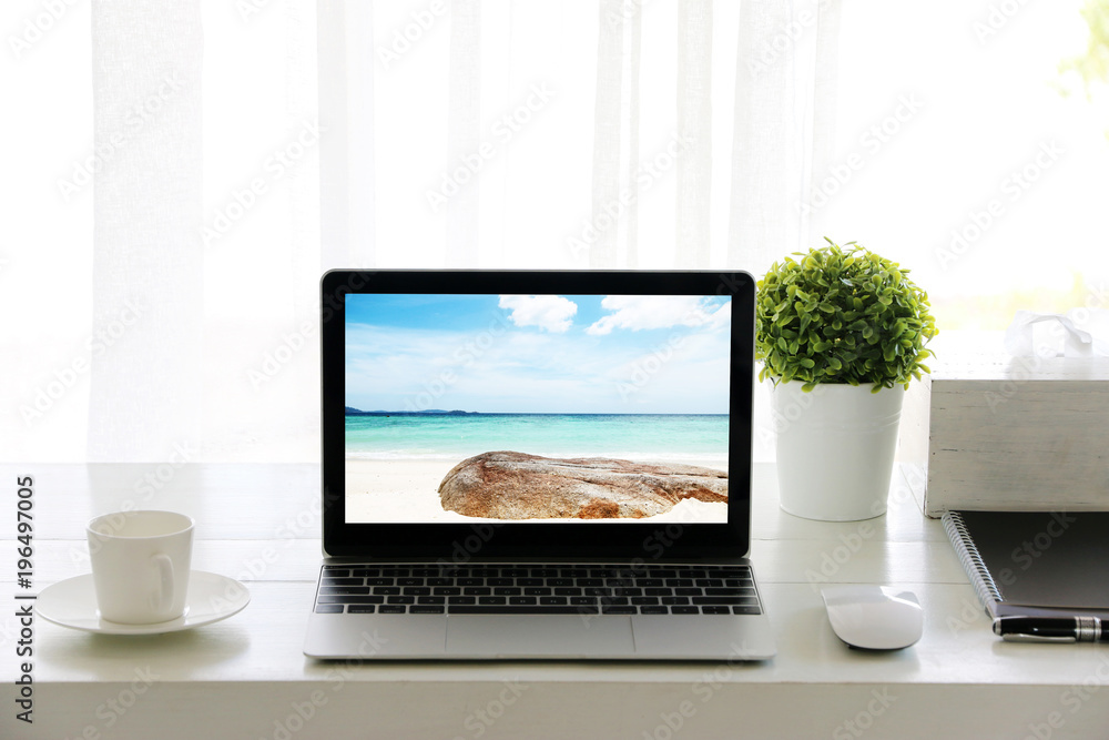 Beach in screen Laptop on table and Coffee cup room Office morning.concept of time relax. Beach in screen Laptop on table and Coffee cup room Office morning.concept of time relax.