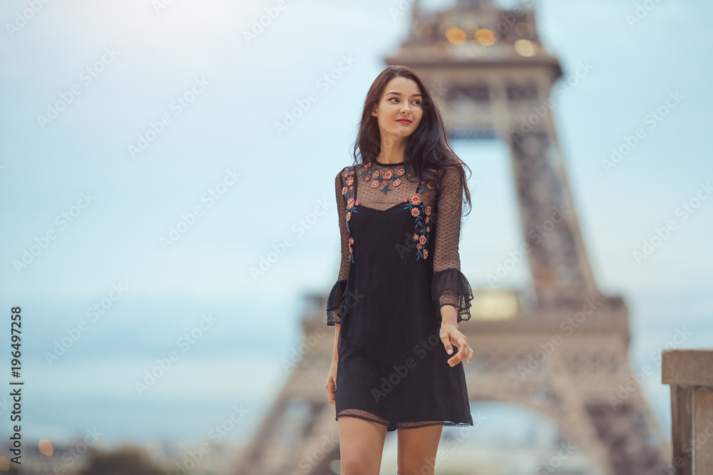 Fototapeta premium Elegancka romantyczna paryżanka w czarnej seksownej sukience z kwiatami spacerująca wieczorem w pobliżu wieży Eiffla w punkcie widokowym Trocadero w Paryżu, Francja. Wspaniała mieszana rasa azjatycka dziewczyna kaukaska korzystających