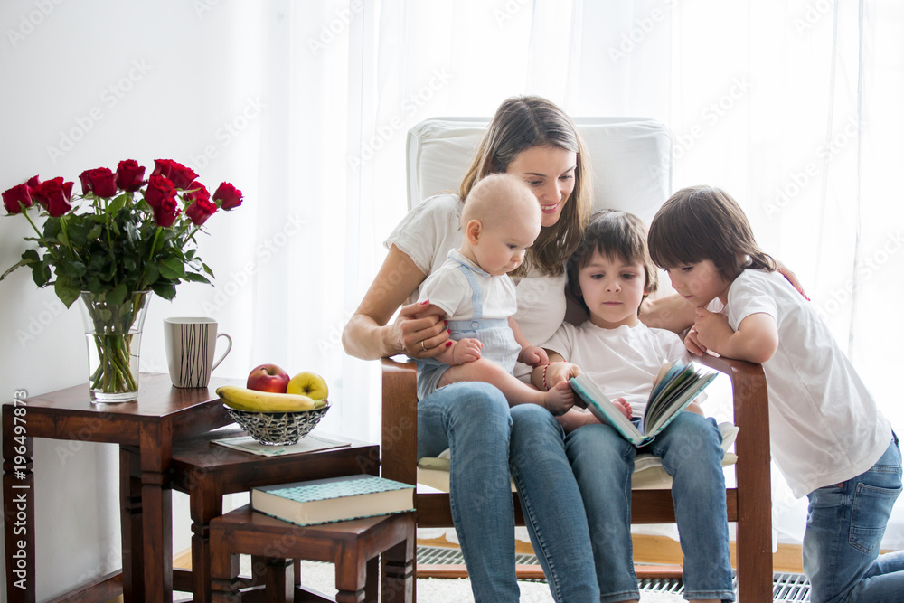 Mother, playing with her toddler boy and his older brother, reading book, smiling Mother, playing with her toddler boy and his older brother, reading book, smiling