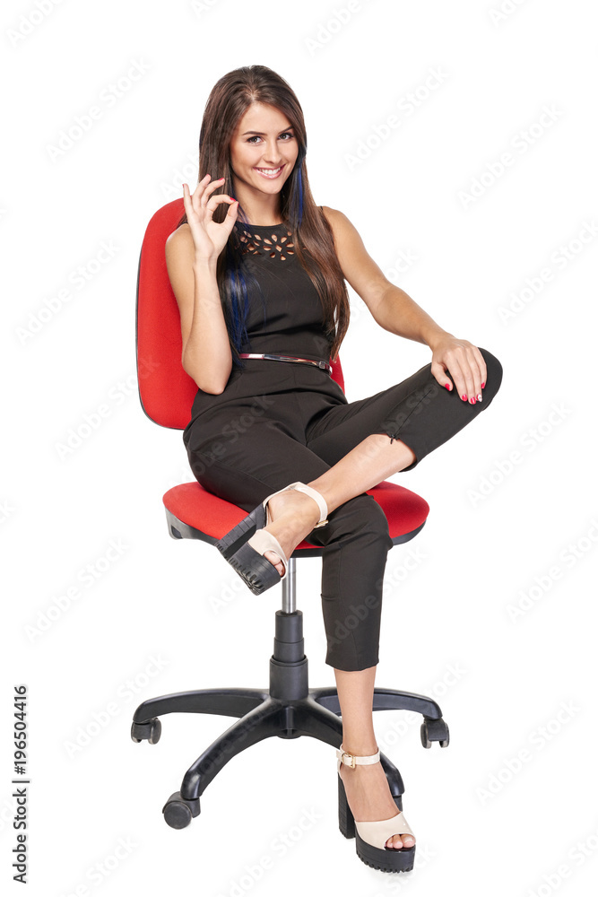 Smiling woman in black sitting on office chair smiling at camera gesturing OK, full length portrait Smiling woman in black sitting on office chair smiling at camera gesturing OK, full length portrait