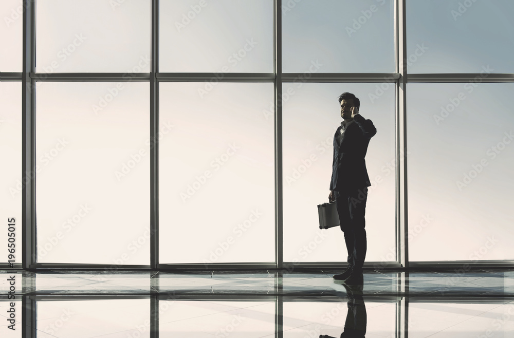 Silhouette view of young businessman is standing in modern office with panoramic windows Silhouette view of young businessman is standing in modern office with panoramic windows