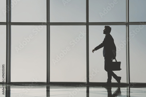 Silhouette view of young businessman is standing in modern office with panoramic windows