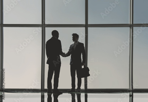 Silhouette view of two young businessmen are standing in modern office with panoramic windows