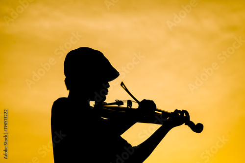 Silhouette boy playing violin with sun set.