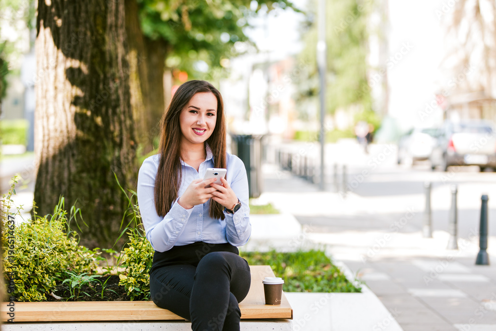 Fototapeta premium Young beautiful businesswoman drinks coffee and use cellphone