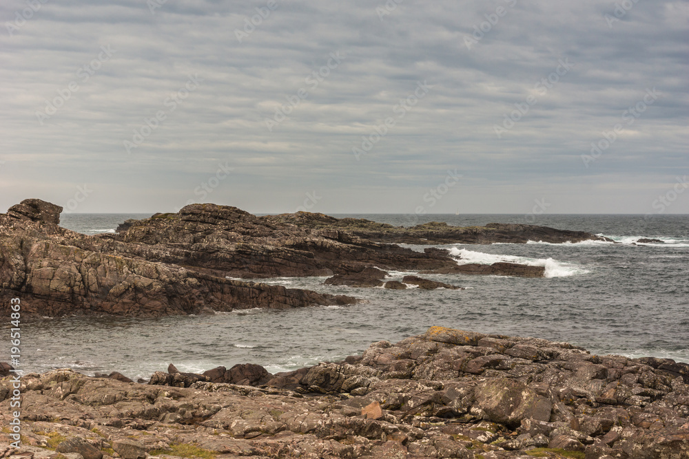 Cove, Scotland - June 9, 2012: End-of-road lookout over Atlantic Ocean showing brown rock formation descending in gray water with surf under cloudy sky.