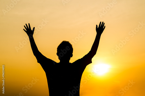 Silhouette boy raising hands with sun set outdoor.