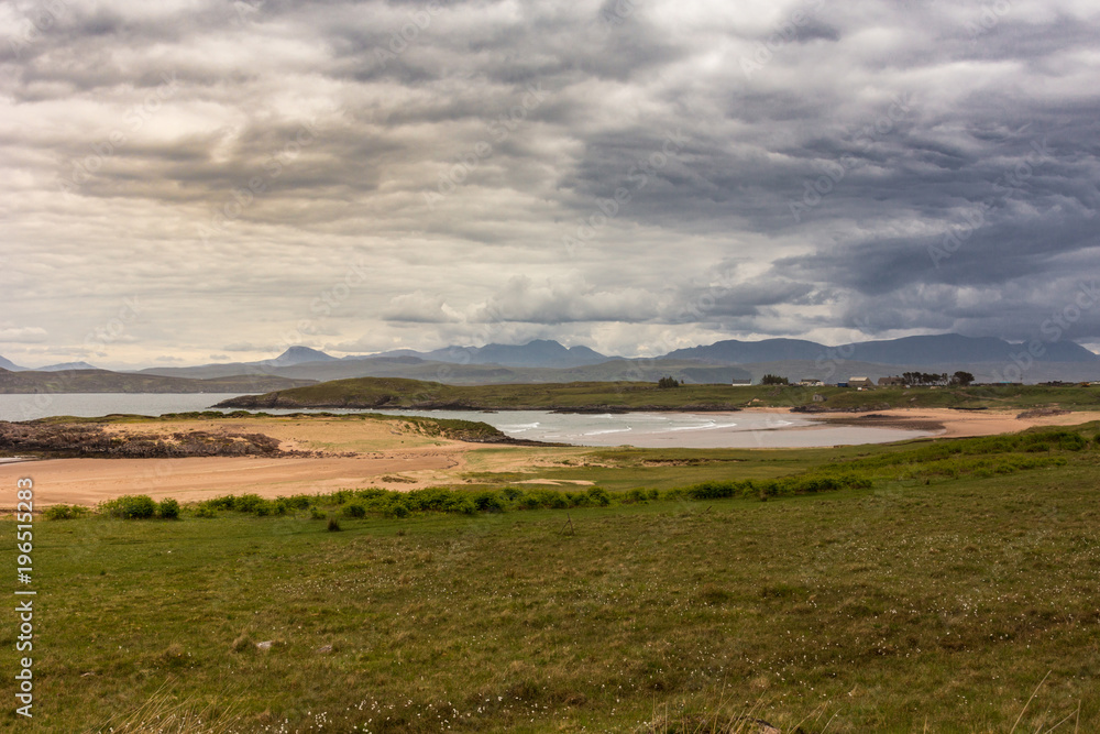 Inverasdale, Scotland - June 9, 2012: Exception brown and gray cloudscape over sandy beach surrounded by green grassland. Farms and dark mountain range on horizon. Inverasdale, Scotland - June 9, 2012: Exception brown and gray cloudscape over sandy beach surrounded by green grassland. Farms and dark mountain range on horizon.