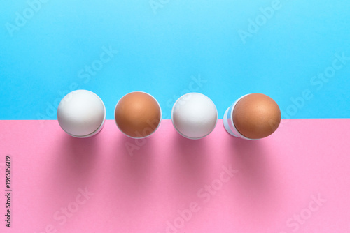 Eggs standing on egg cup on blue and pink pastel background, copy space. Boiled eggs in stand on paper background with two tone color. Healthy food concept. Easter eggs. Flat lay, top view