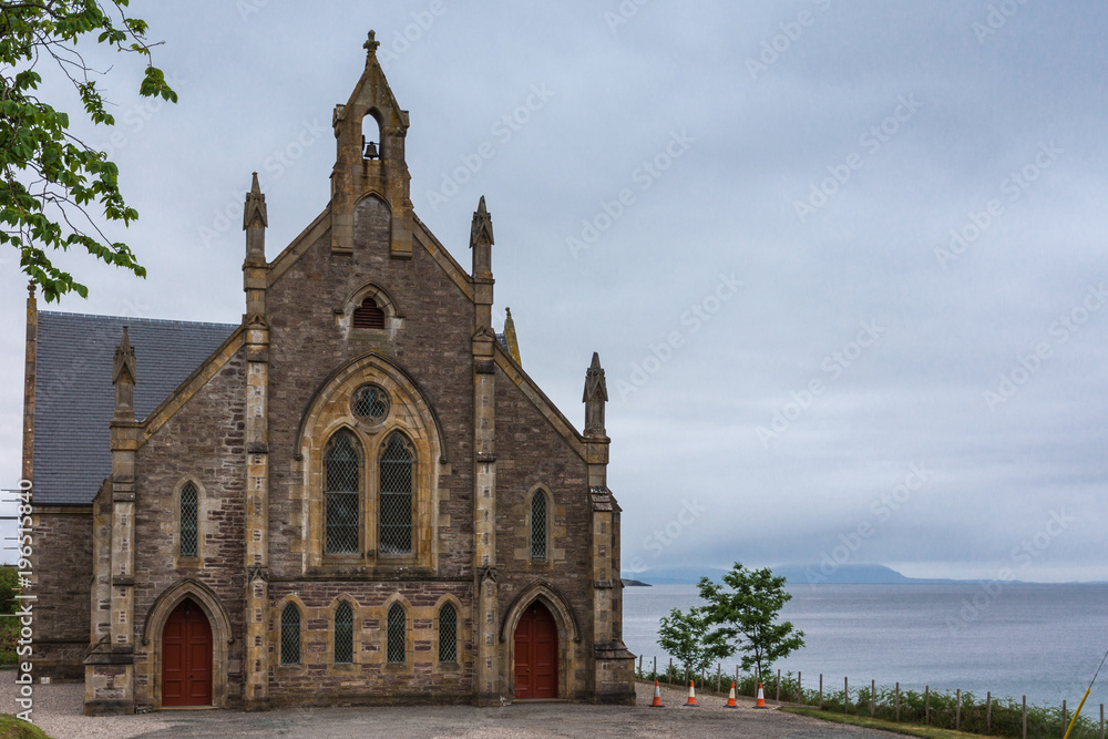 Gairloch, Scotland - June 10, 2012: The Free Church of Scotland brown stone building on the shore of the blue-gray Atlantic Ocean. Light blue sky. Vegatation adds green.