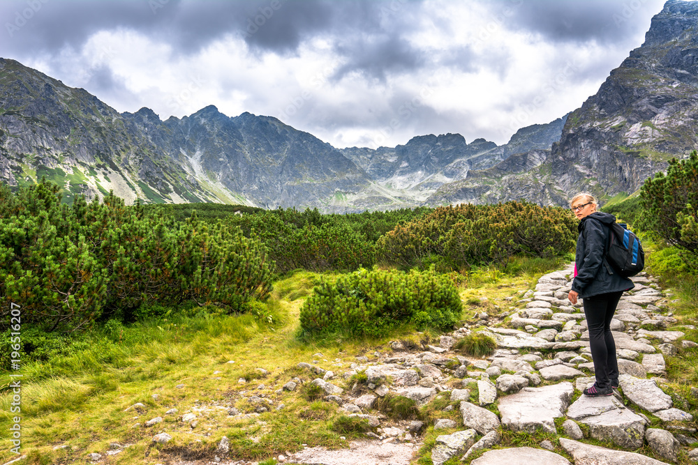 Hiker woman on mountain trail hiking with backpack, path with stones in high mountains, panoramic landscape