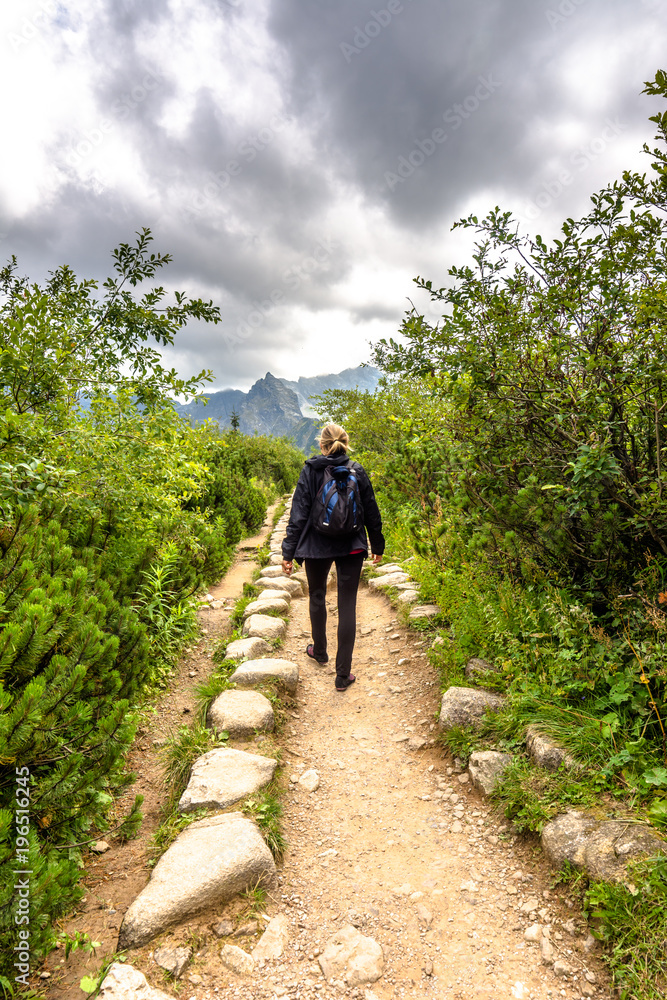 Woman hiker on mountain trail hiking with backpack in mountains, landscape Woman hiker on mountain trail hiking with backpack in mountains, landscape