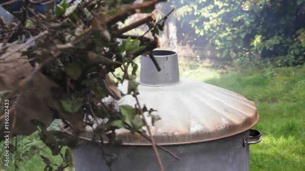 Domestic garden incinerator, a man adds garden waste to a smokey