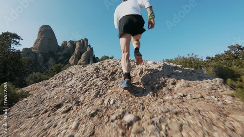 Low angle slow motion action sports shot of strong and muscular man in sports outfit run up steep rock or cliff during ultra marathon trail running workout training or competition in epic landscape.