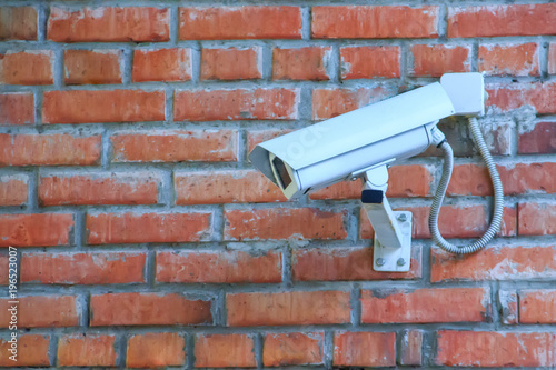 Stationary outdoor video camera in a thermal housing of a security video surveillance system on a brick wall.
