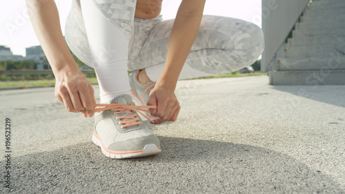CLOSE UP: Unrecognizable young fit woman is tying up her sneaker shoelaces.