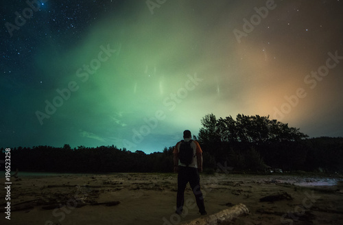 Light pillars rise above trees with rear view of a man standing witness it. soft focus, blur and noise due to long expose and high iso.