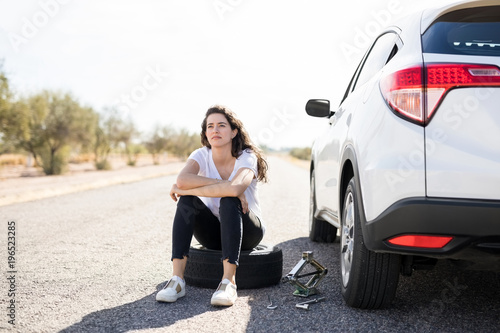 Woman looking upset with flat tyre on her car © AntonioDiaz