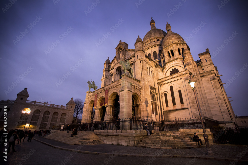 The Sacre Coeur Basilica shine bright in the winter night, atop a hill in the Montmartre neighborhood of Paris, France.