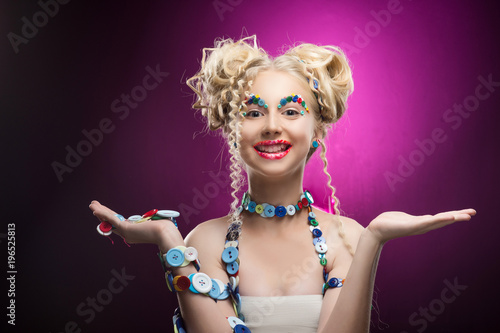 Smiling cute face nice blonde child girl wearing DIY bijou accessories made of multi-colored buttons holds blank copy space on her palms.