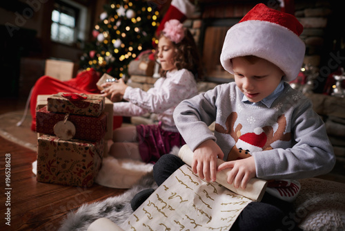 Young girl and boy sorting Christmas gifts, young boy rolling list photo