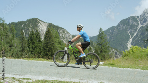 Cheerful cyclist riding his electric bicycle up a hill in the sunny mountains.