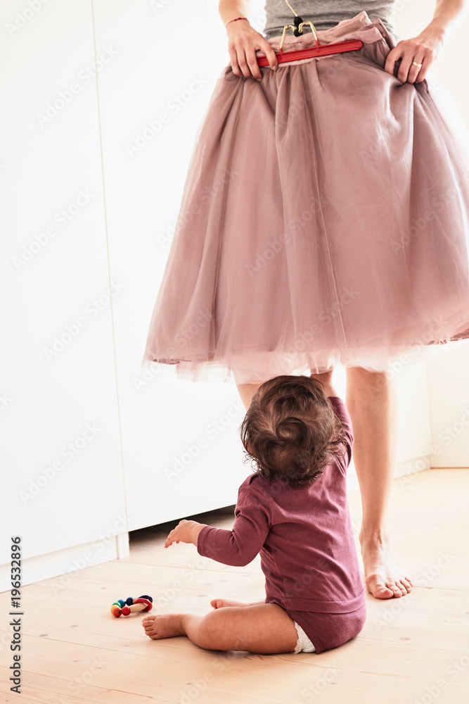 Mother holding skirt up against her, baby girl sitting on floor watching  her, low section Stock Photo | Adobe Stock