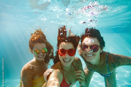 Cheerful friends making selfie underwater in pool