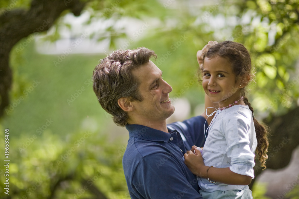 Portrait of a smiling young girl being held by her father while outside in the garden. Portrait of a smiling young girl being held by her father while outside in the garden.