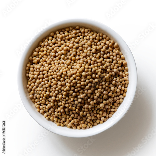 Dried white mustard seeds in white ceramic bowl isolated on white from above.