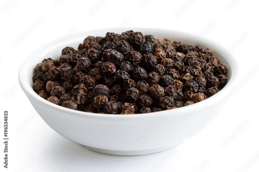 Whole black peppercorns in white ceramic bowl isolated on white.