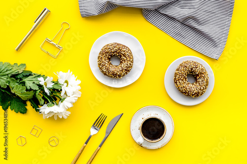 modern breakfast desing with sweet donut, coffee and flowers on woman yellow desk background top view photo