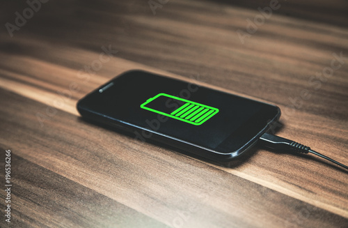 Mobile phone charging on wooden desk.