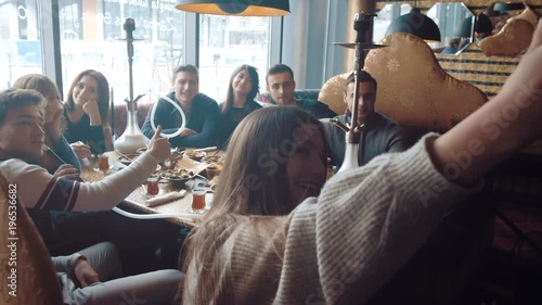 Young company is making selfie. Smoking a hookah and communicating in an oriental restaurant.