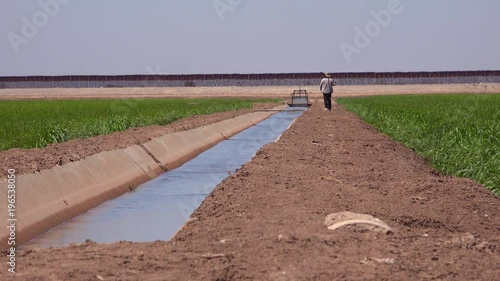 A farmer walks along the US Mexico border with the wall in the background.