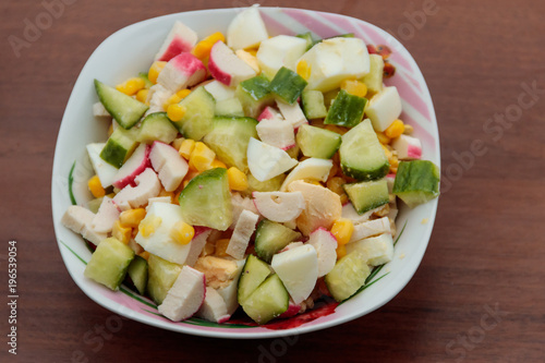 Salad with crab sticks, sweet corn, cucumber and eggs on wooden table
