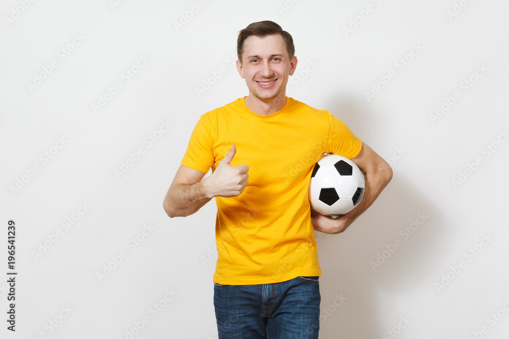 Inspired young European man, fan or player in yellow uniform hold soccer ball, show thumb up, cheer favorite football team isolated on white background. Sport play football, healthy lifestyle concept.