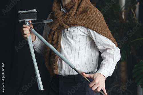 a man in a white shirt and a brown sweater is holding an old tripod with a camera, a vintage photo