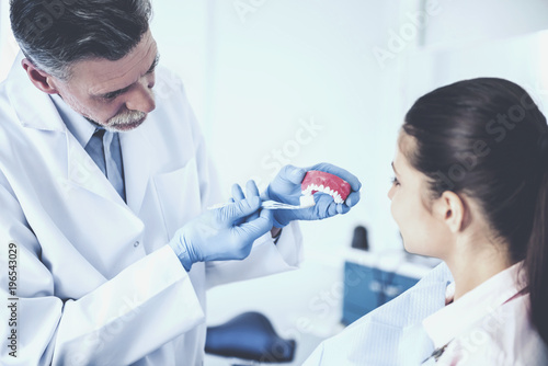 Cheerful dentist teaching on model of human teeth how right to brush teeth his female patient