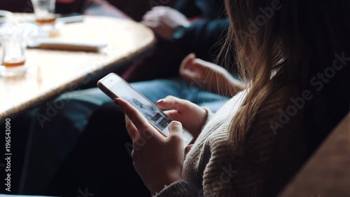 Young beautiful girl is surfing internet on phone in bar.