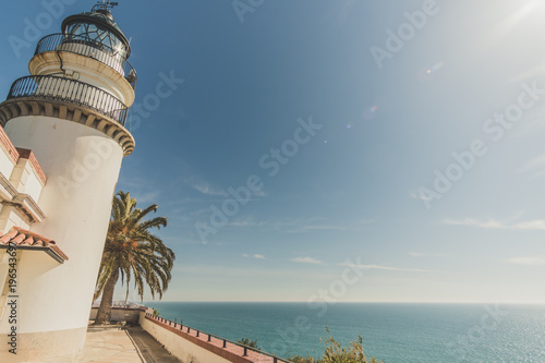 A lighthouse in front of the calm waters of the mediterranean sea. It's a sunny day in the coast of Calella in Catalonia, Spain. photo